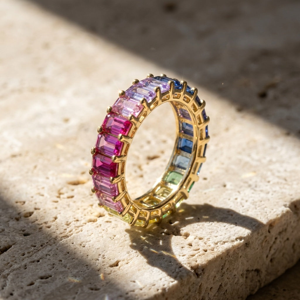 Gold 3x5mm emerald cut rainbow eternity band ring standing on travertine stone slab under natural sunlight