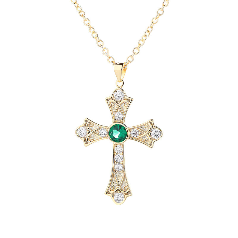 Gold cross pendant with a green gemstone on a white background