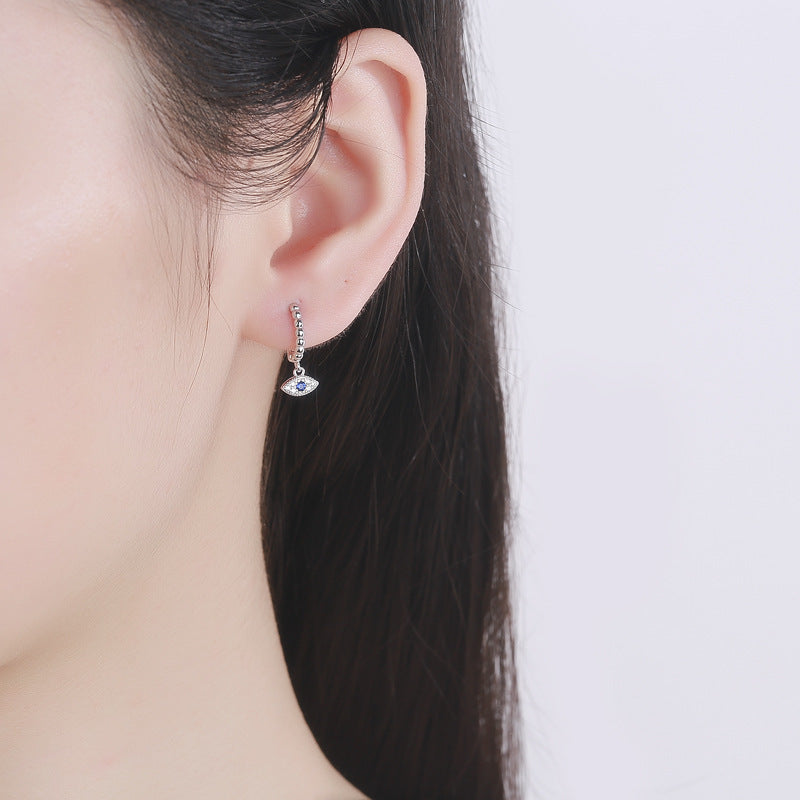 Macro of evil eye charm on mini hoop. Alt: “Blue Enamel Evil Eye Detail – Sterling Silver Huggies.”