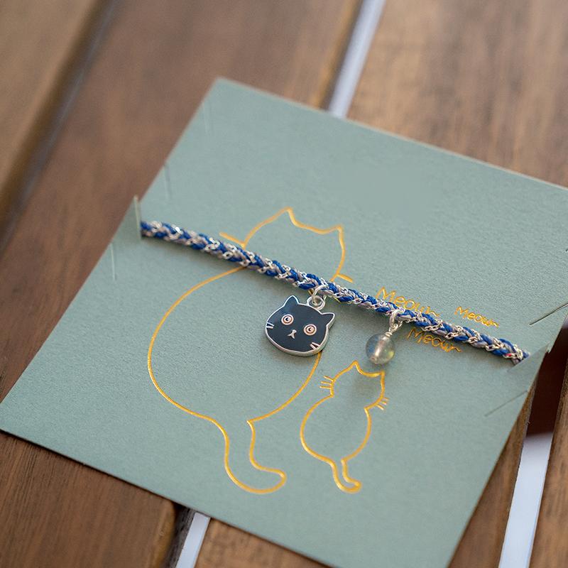 Bracelet with a cat charm on a green card with a cat illustration, placed on a wooden surface.