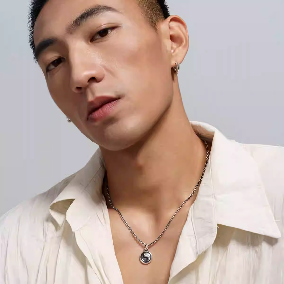 Man wearing a white shirt and necklace against a light gray background