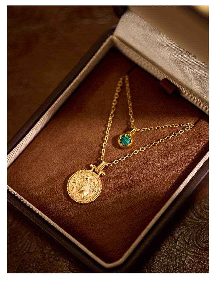 Two gold necklaces with pendants on a brown velvet surface