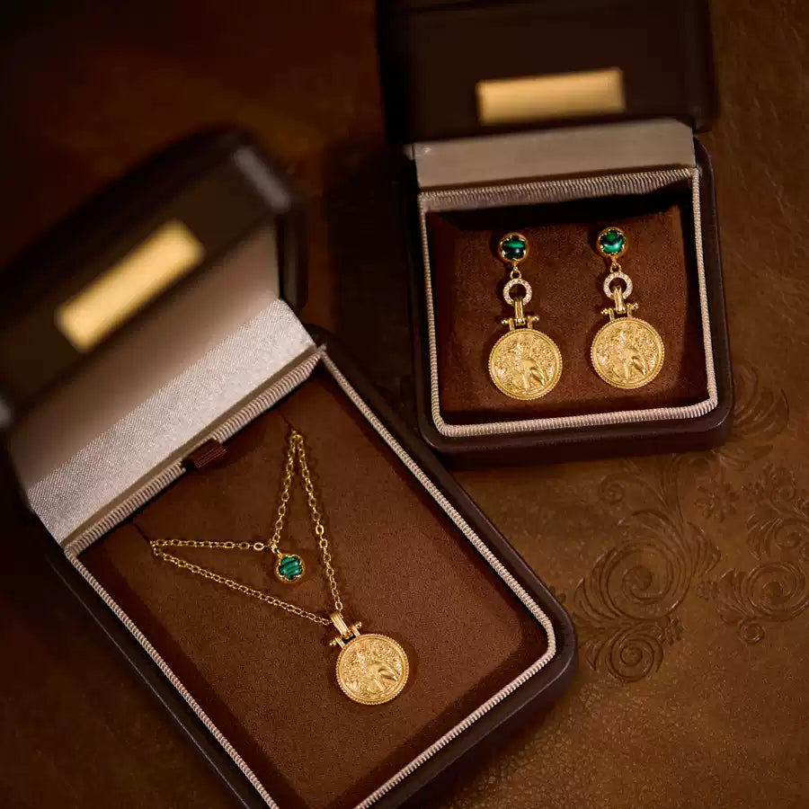 Gold necklace and earrings with green gemstones in brown jewelry boxes.