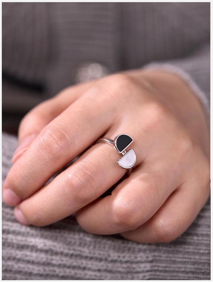 Close-up of a hand wearing a ring with a black and white stone on a gray background