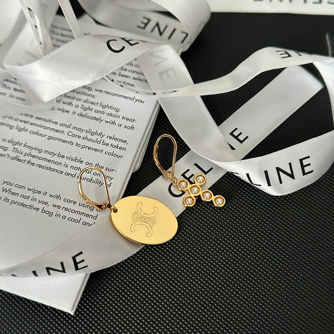 Gold-tone jewelry set featuring a round engraved disc charm and a dangling floral cluster charm with clear rhinestones, displayed on a white branded ribbon over printed paper on a dark textured surface.