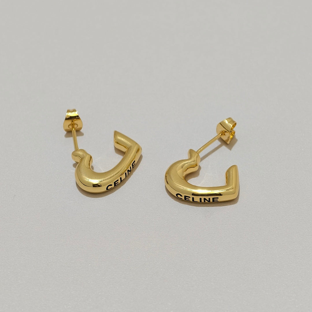 A pair of gold Celine huggie hoop earrings with the brand name engraved on the front, displayed on a neutral light gray background.