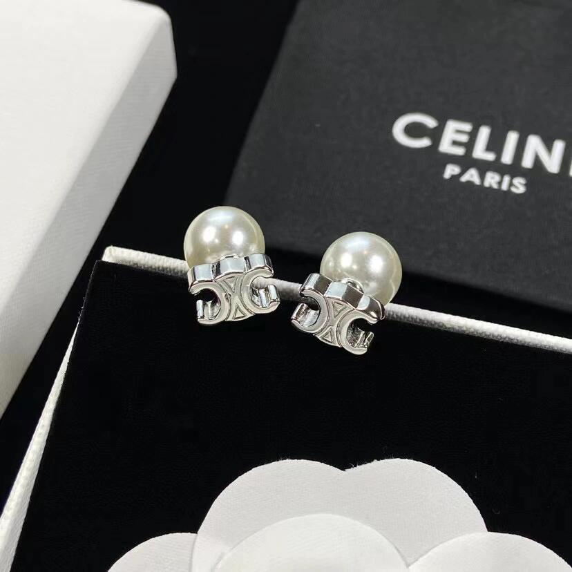 A pair of Celine pearl stud earrings with silver-toned logo clasp backs, displayed on a black velvet jewelry box with a white box and black Celine Paris packaging visible.