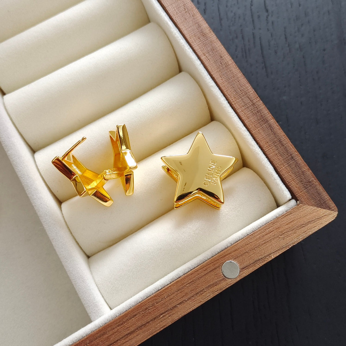 A pair of gold-toned cufflinks, including a star-shaped clasp and a butterfly-shaped clasp, displayed inside an open wooden jewelry box with cream velvet cushions.