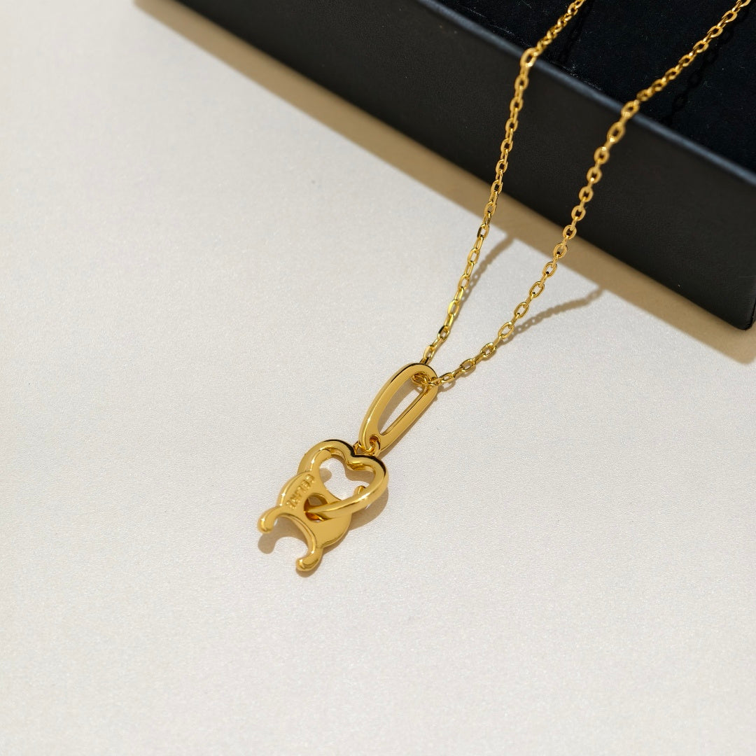 A gold pendant necklace featuring a stylized elephant and heart design, resting on a light beige surface with a black display box in the background.