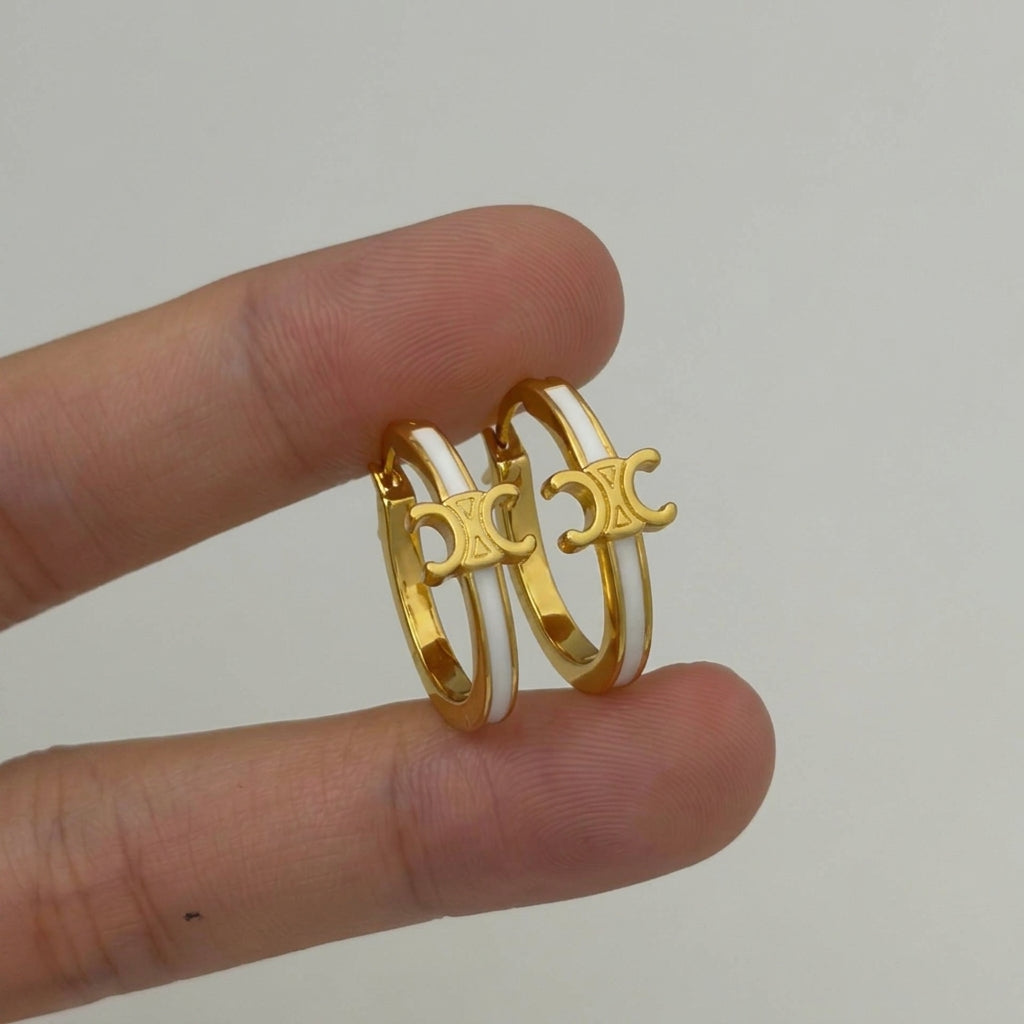 A pair of gold hoop earrings with a double-C logo design, held between two fingers to show scale against a plain light gray background.