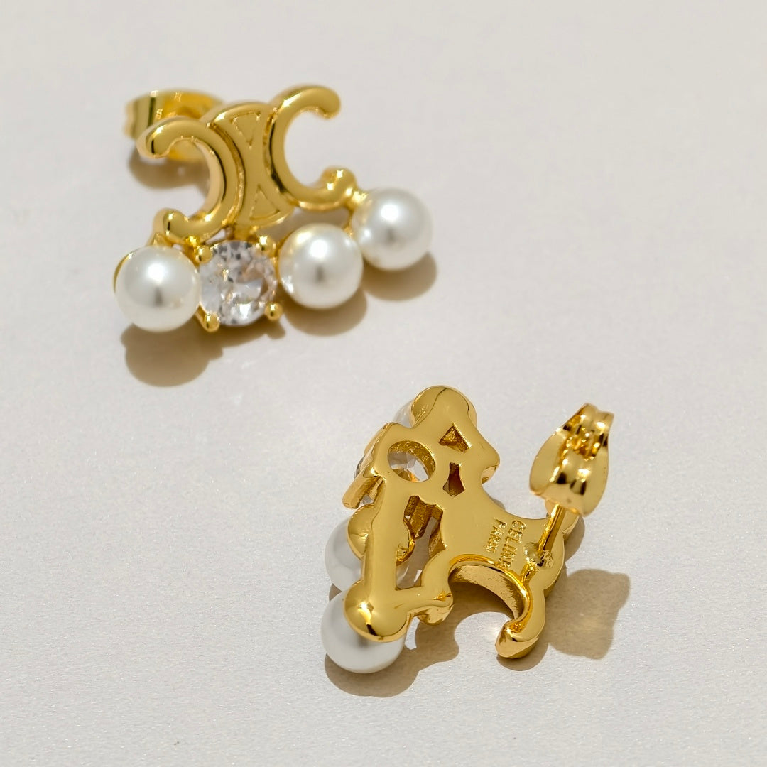 A pair of gold-toned clip-on earrings with white faux pearls and a clear central crystal, displayed on a light beige background.