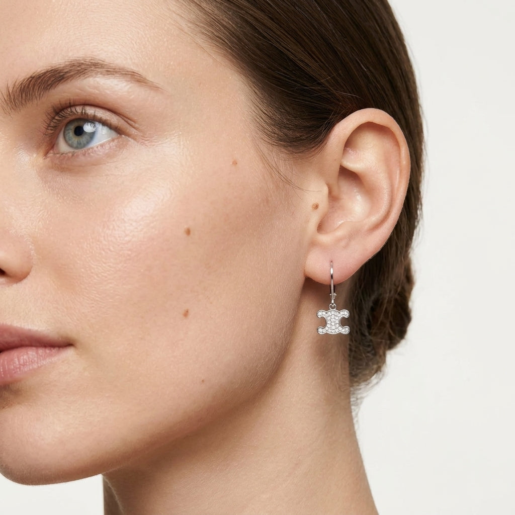 A close-up of a woman's ear wearing a silver double-C logo dangle earring, set against a clean, light off-white background.