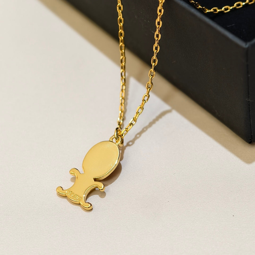 A gold-plated pendant necklace featuring a stylized cartoon character, displayed on a light beige surface next to a black box.
