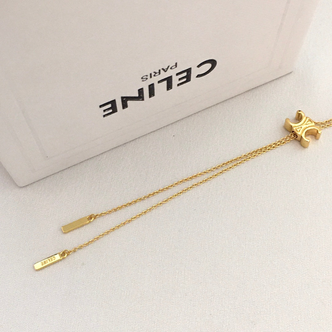 A gold-tone Celine bracelet with a signature monogram 'C' charm, a flat bar pendant, and a small engraved tag on a delicate chain, displayed next to its white Celine Paris box.