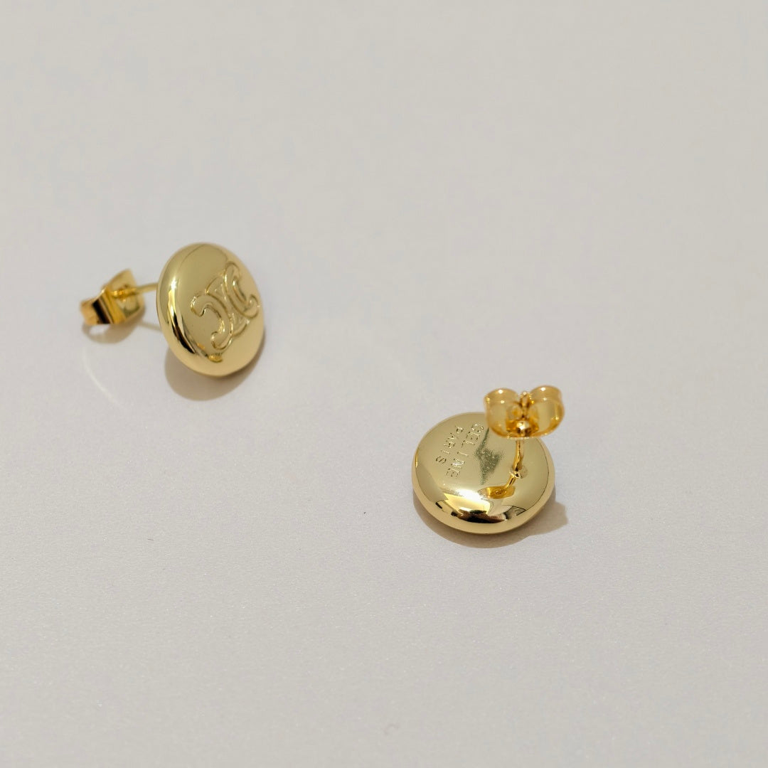 A pair of gold round stud earrings with a raised monogram design, shown from the back on a light gray background.