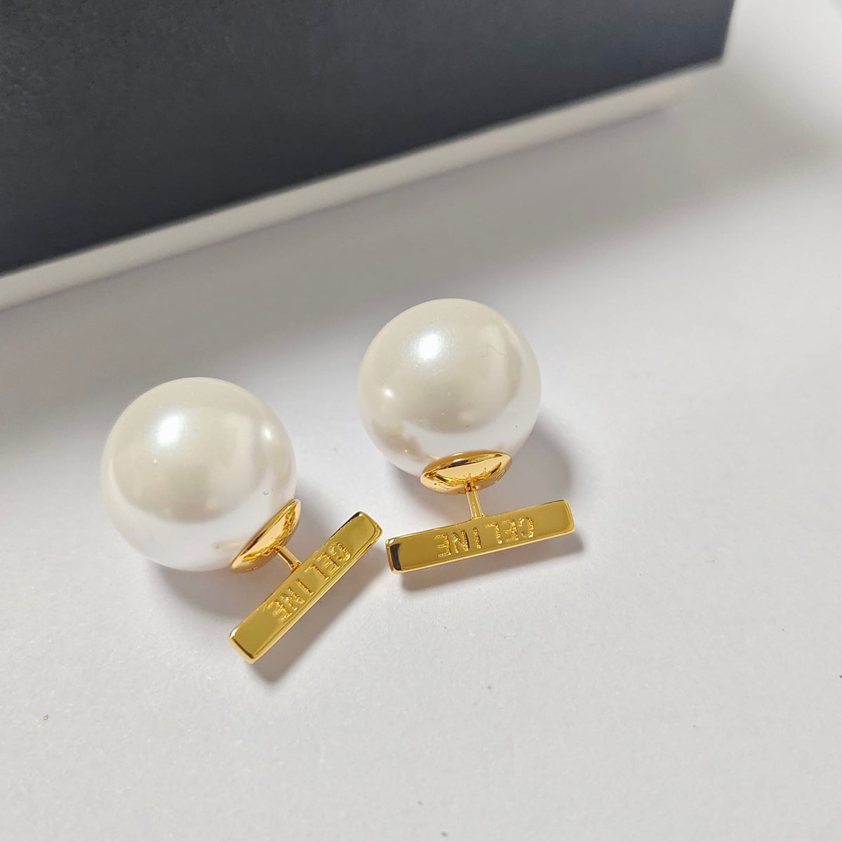 A pair of gold and white pearl stud earrings with rectangular gold bar backings, displayed on a light gray surface.