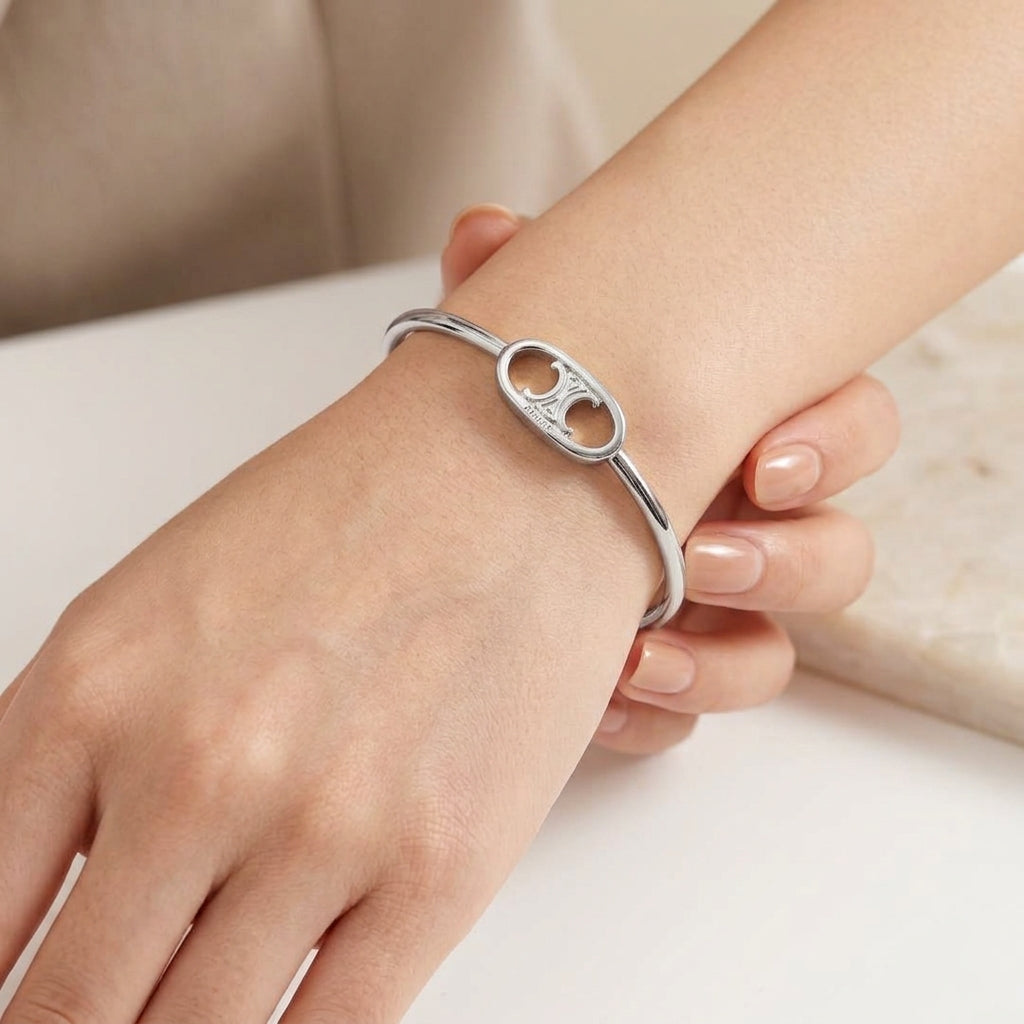 A close-up of a person's wrist wearing a polished silver bangle bracelet with a double oval cutout design.
