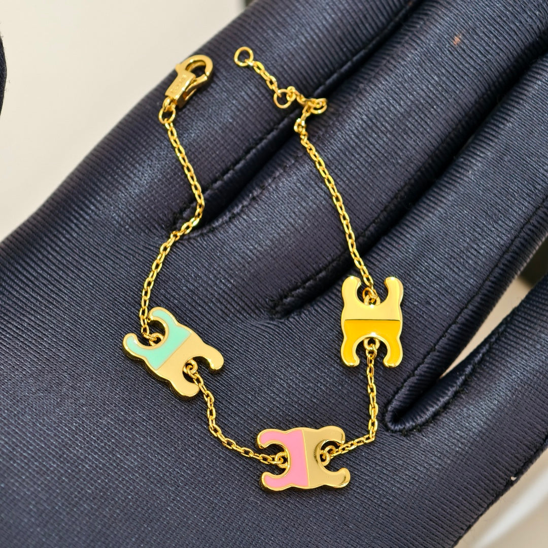 A gold chain bracelet with three interlocking C-shaped charms in pastel mint green, yellow, and pink, displayed on a dark navy textured fabric surface.