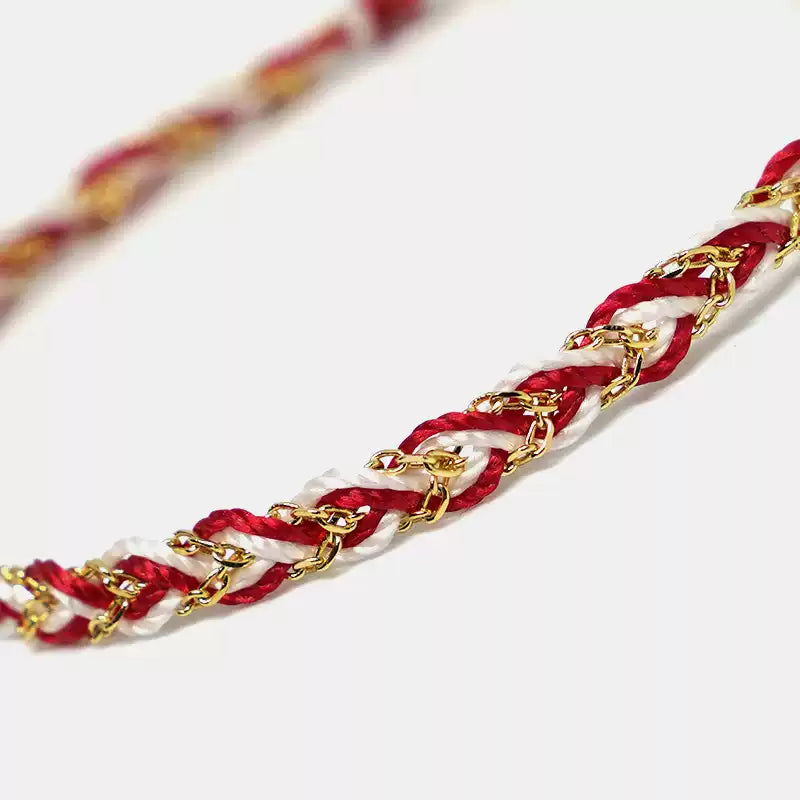 Bracelet with red and white braided cord and gold chain on a light background