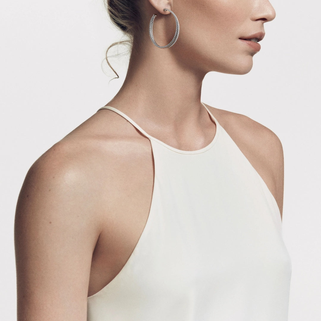 Woman wearing a white tank top and silver hoop earrings on a light background