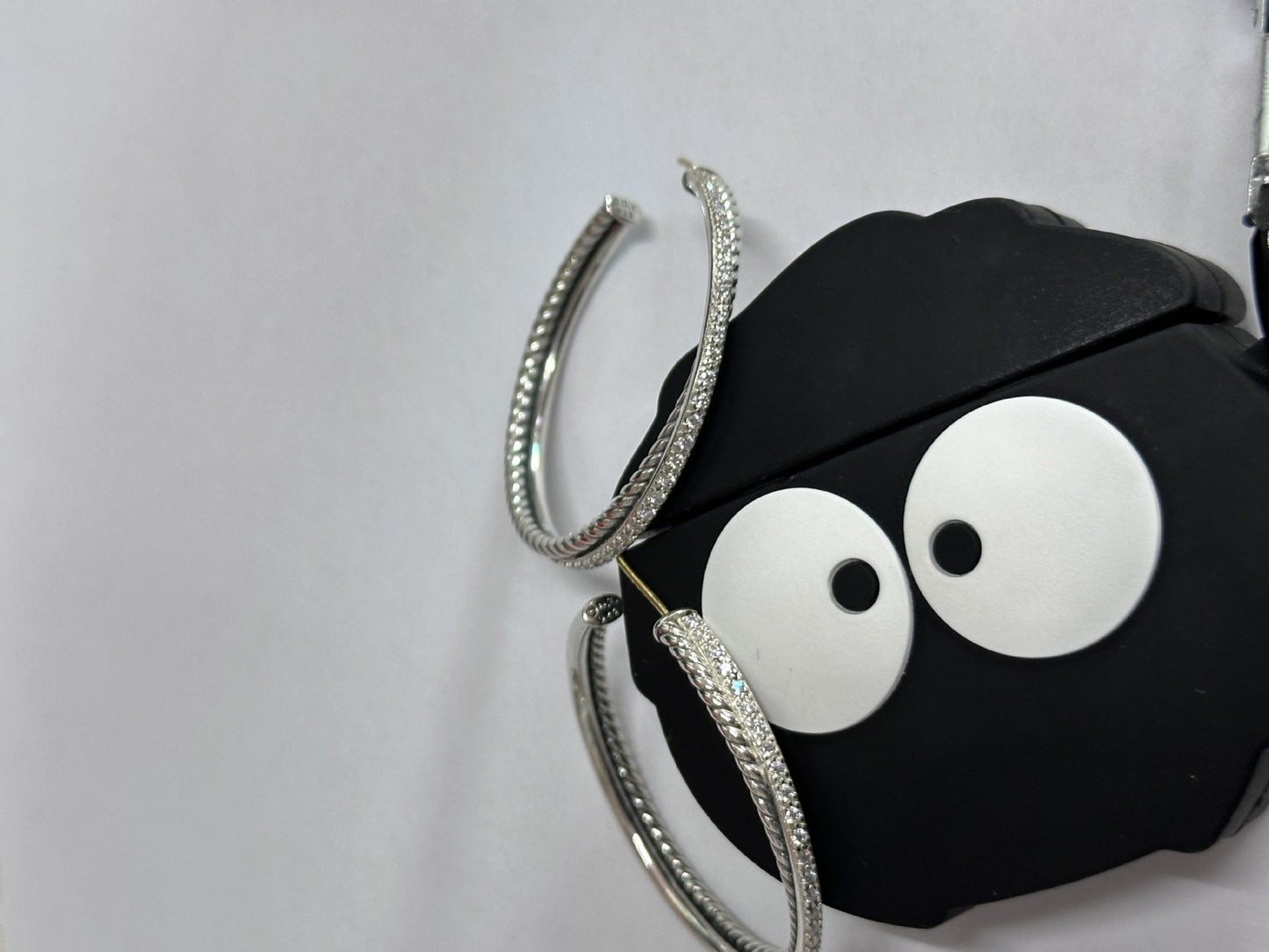 Black airpod case with googly eyes and silver hoop earrings on a white background