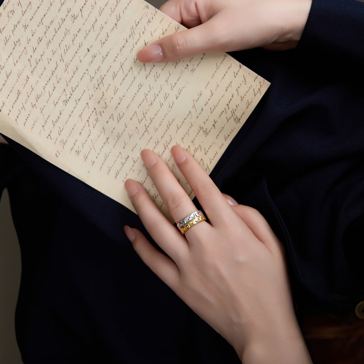 Person holding an open book with a hand wearing a ring on a dark background