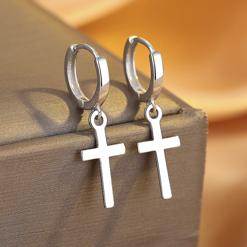 Silver hoop earrings with cross pendants on a textured surface