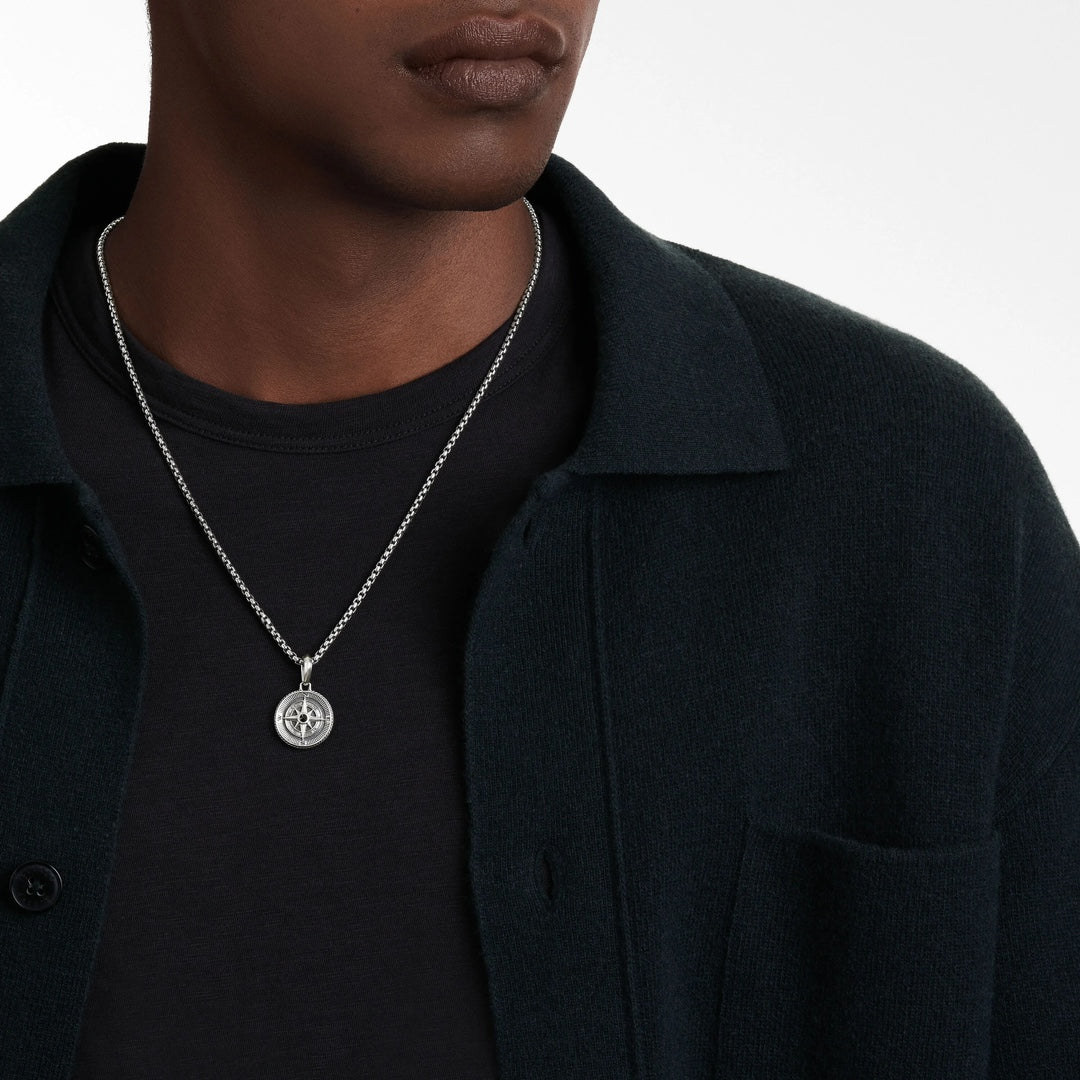 Person wearing a silver necklace with a pendant on a plain background