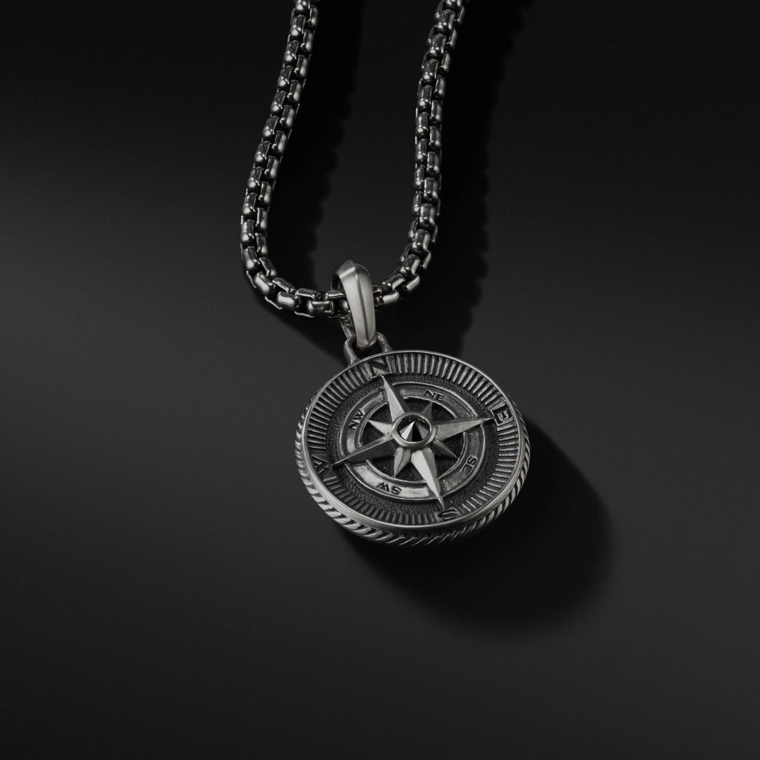 Silver compass pendant on a black chain against a black background