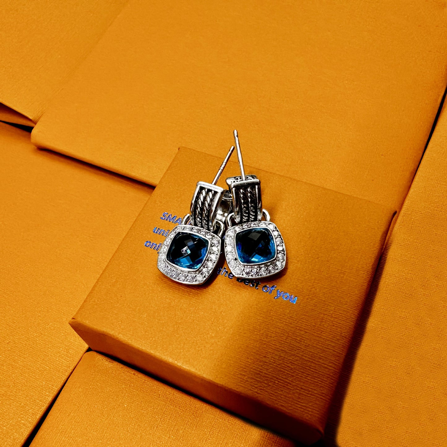 Pair of silver earrings with blue gemstones on an orange fabric background