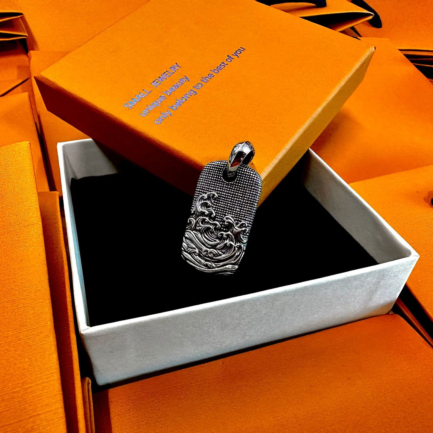 Silver dog tag pendant in an open orange box with text
