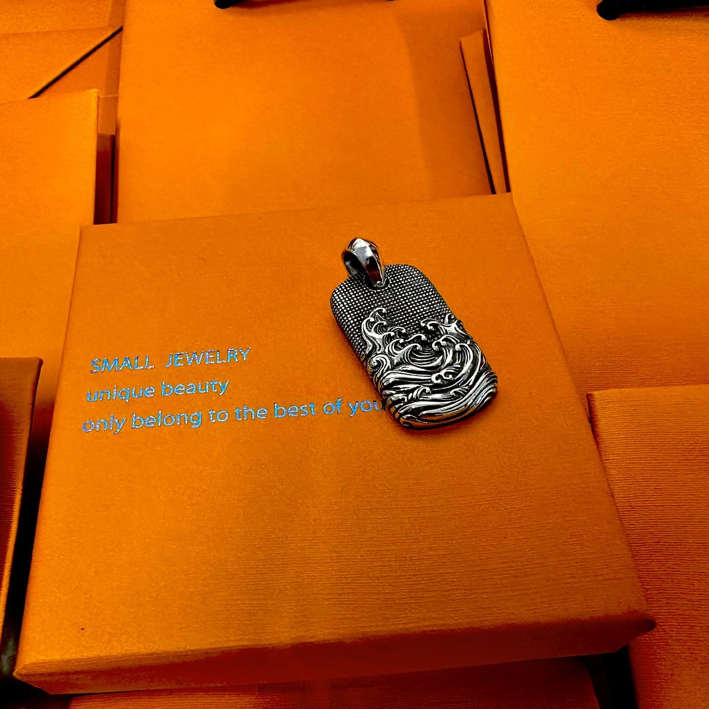 Silver pendant on an orange jewelry box with text