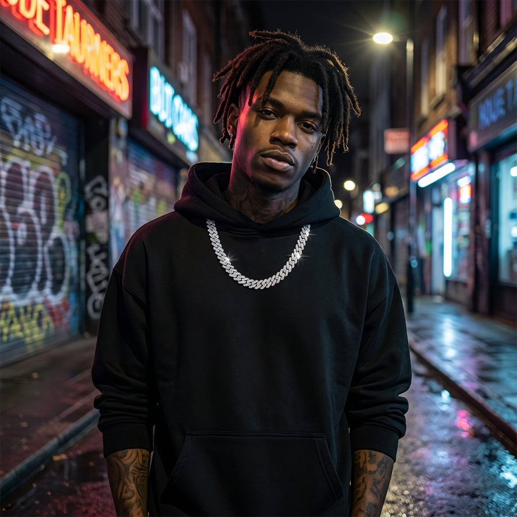 Man wearing a black hoodie with tattoos standing on a neon-lit street.