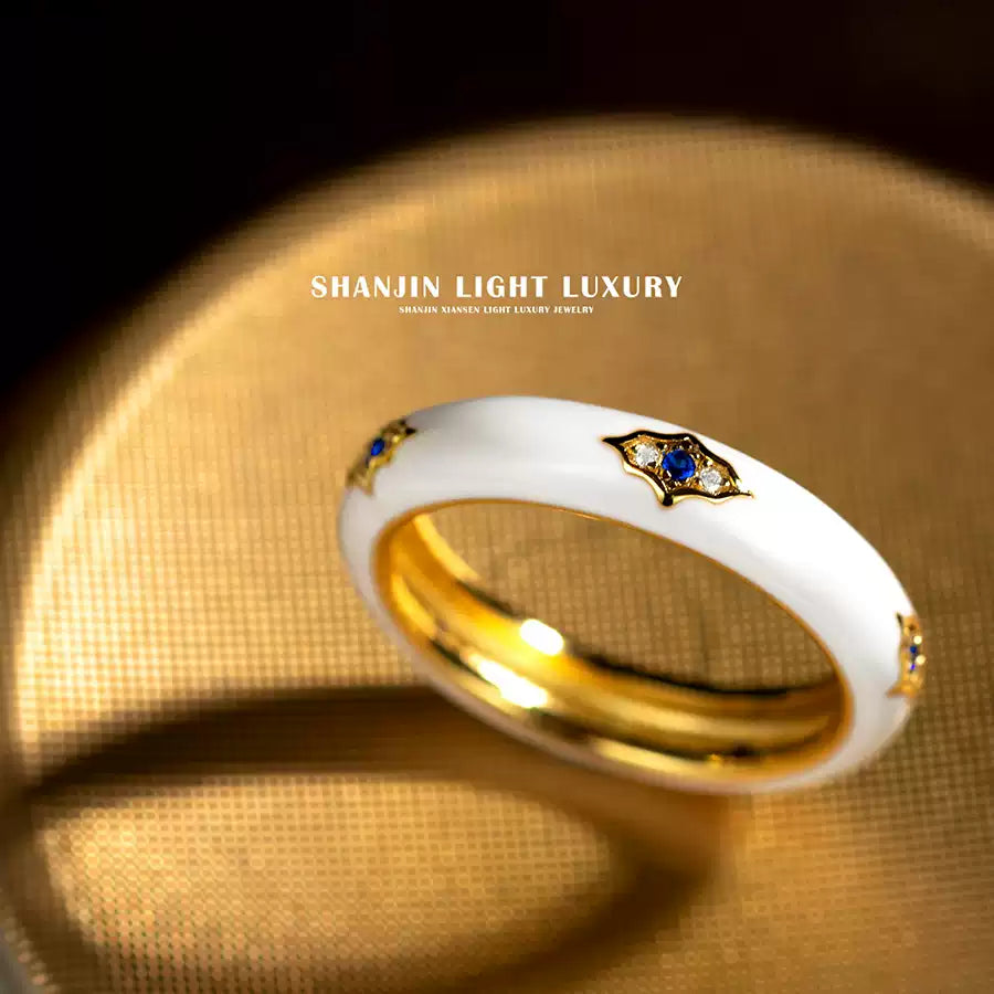 Gold and white ring with blue gemstone on a gold background, featuring Shanjin Light Luxury branding.