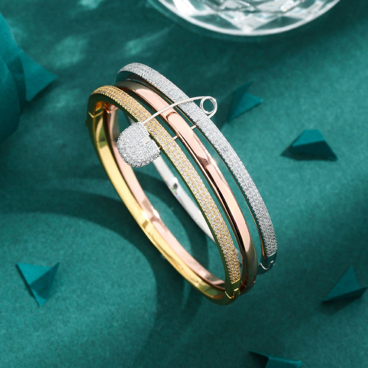 Three gold bangles on a green textured surface with a diamond in the background