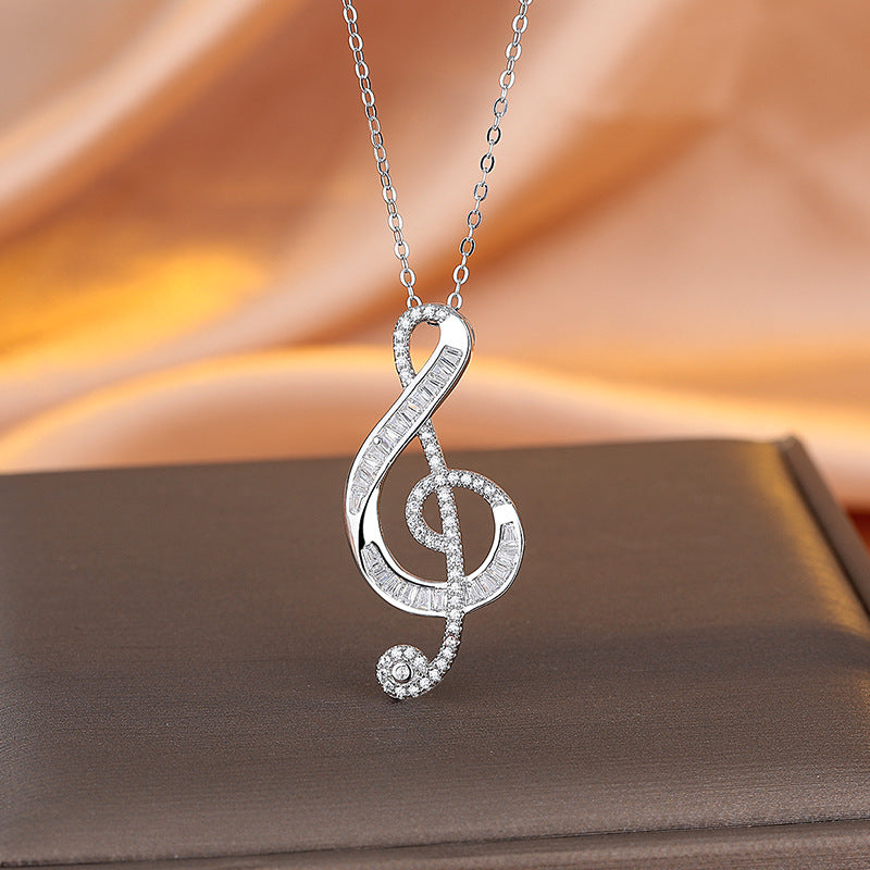 Silver treble clef necklace on a brown surface with a soft orange background