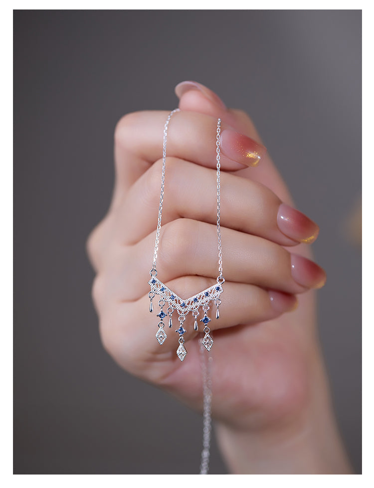 Hand holding a silver necklace with a detailed pendant against a neutral background