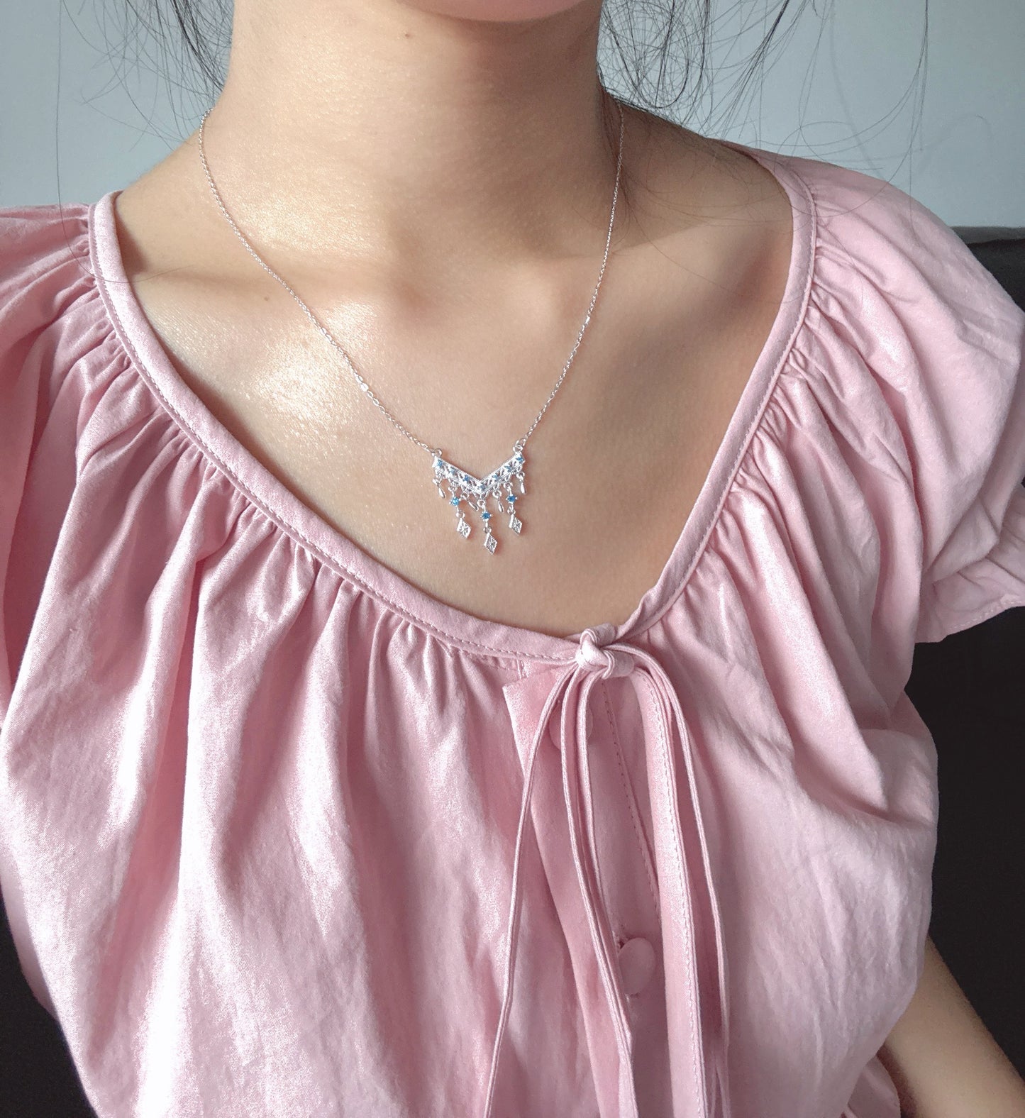 Person wearing a pink top and a silver necklace with a floral pendant.