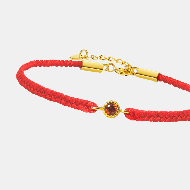 Red braided bracelet with gold clasp and gemstone on a white background