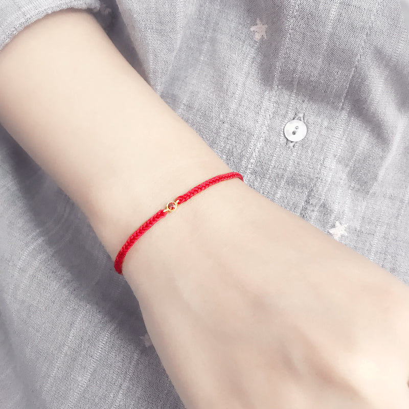 Red string bracelet on a wrist with a gray shirt background