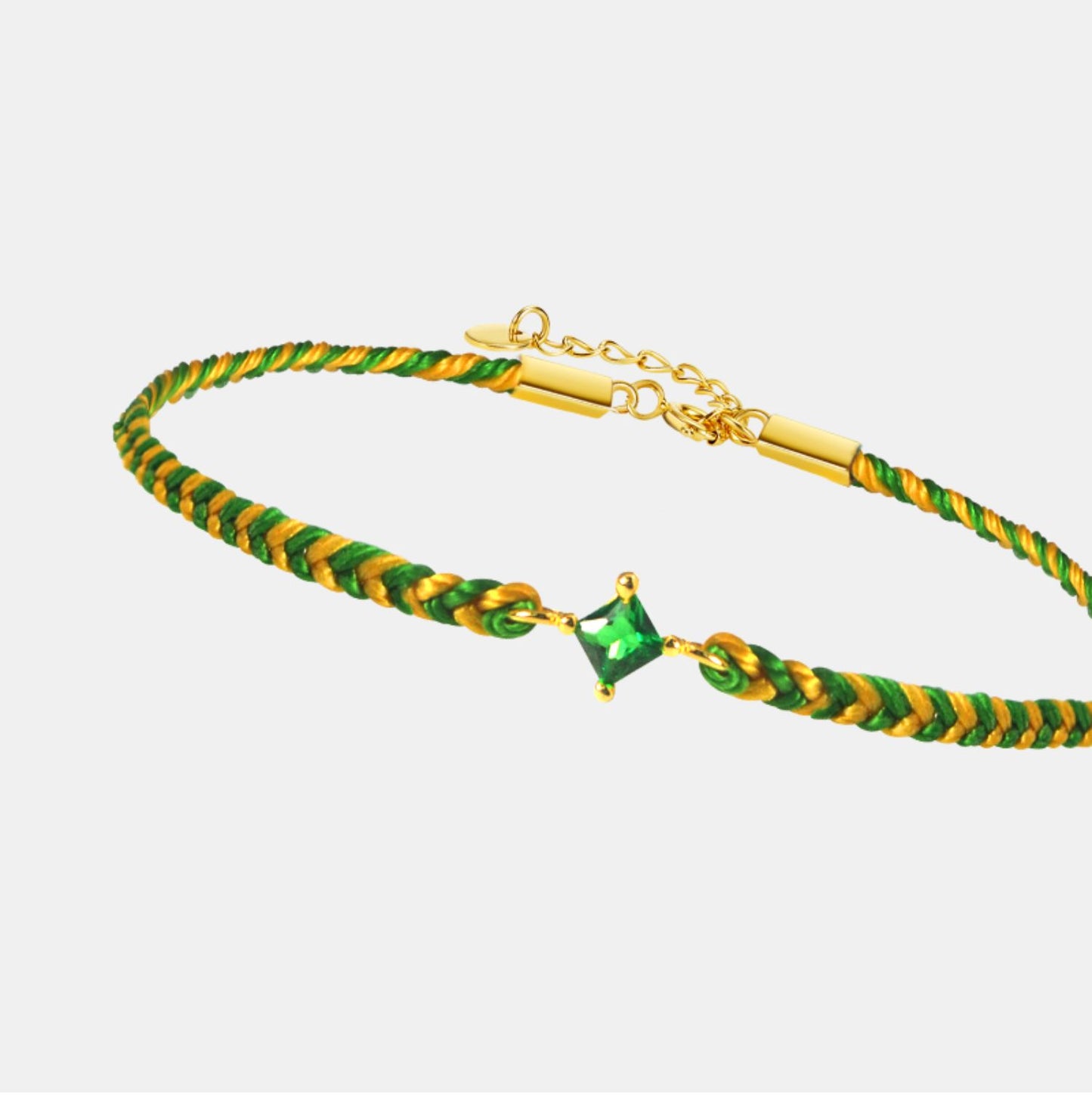 Gold and green braided bracelet with a green gemstone on a light gray background