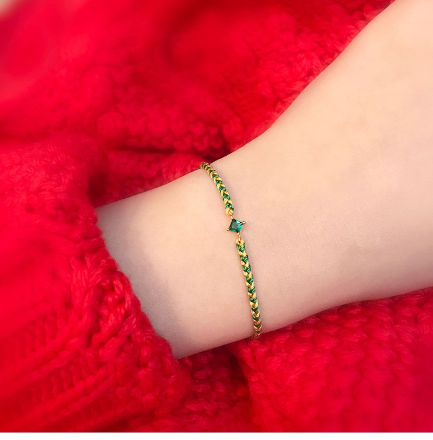 Gold bracelet with green stones on a wrist against a red fabric background