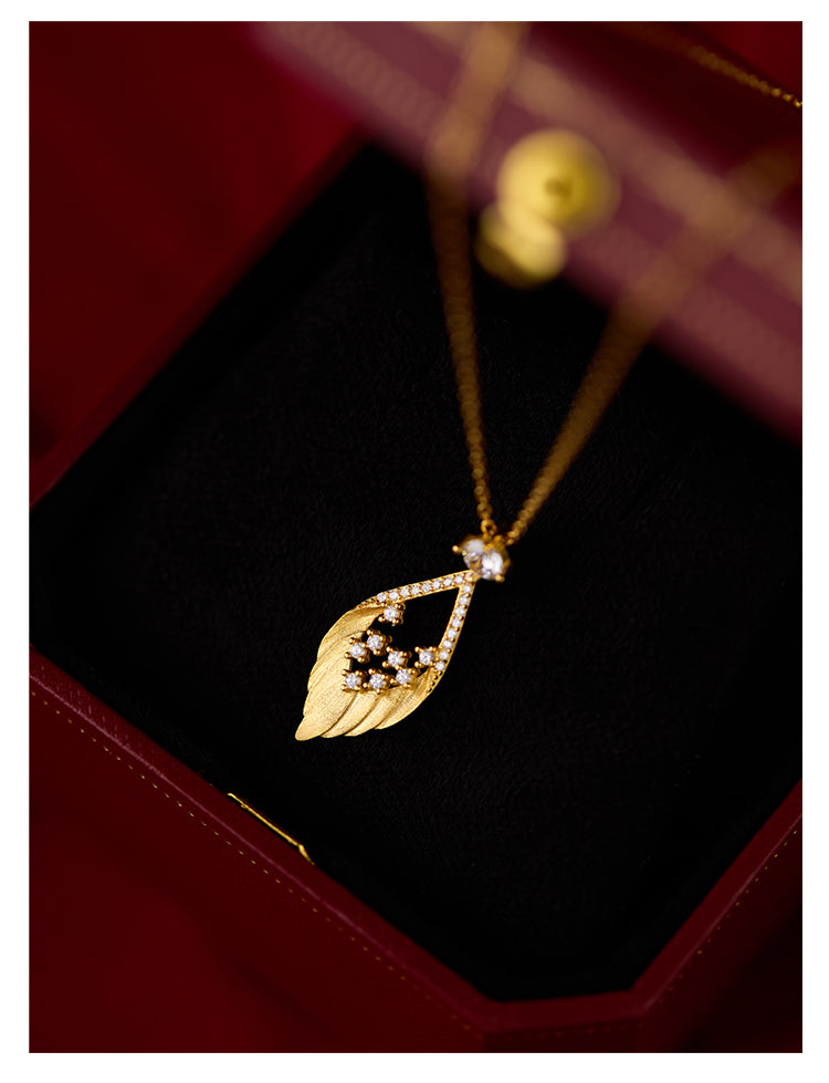 Gold necklace with a leaf-shaped pendant on a dark surface