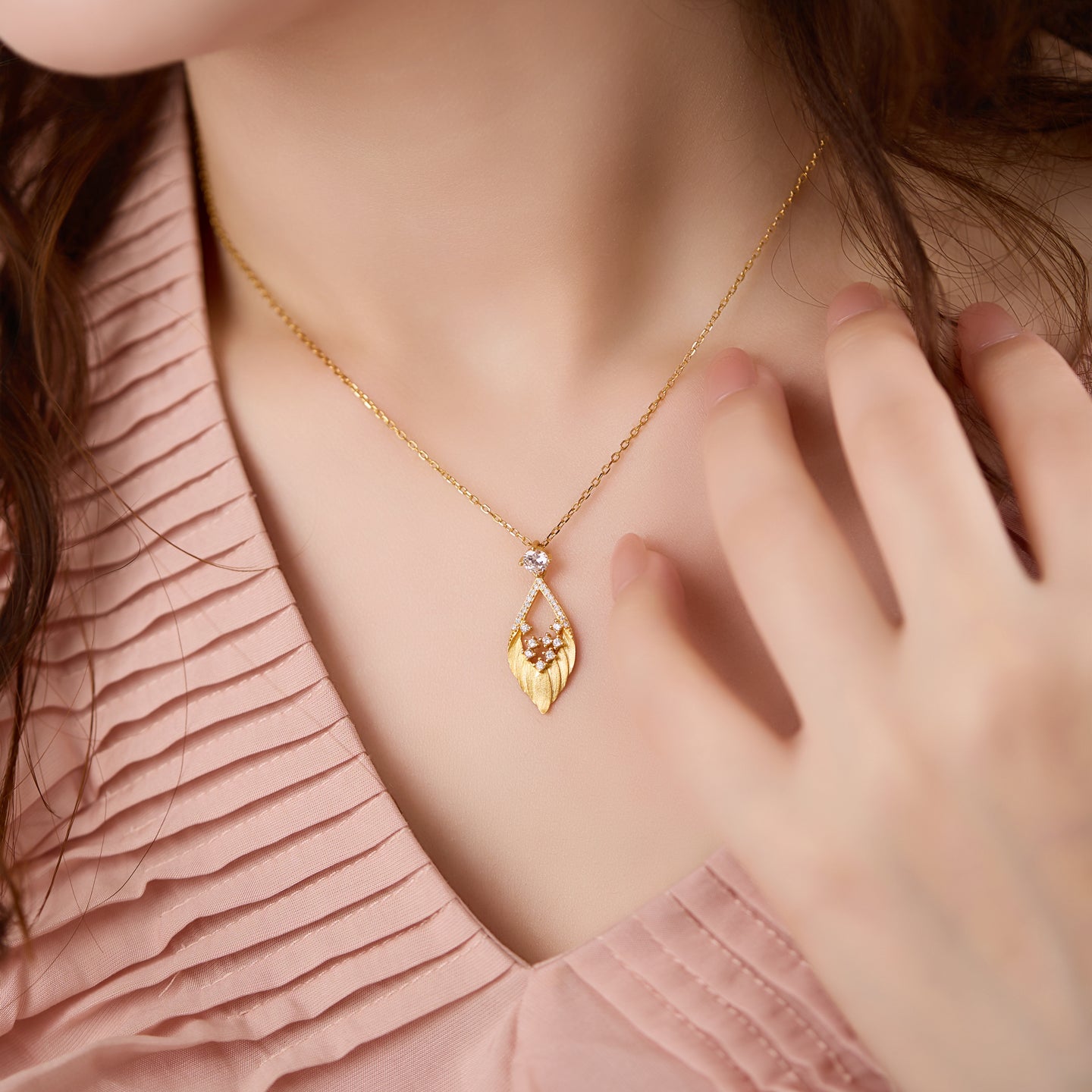 Gold necklace with a heart-shaped pendant worn by a person in a pink top.
