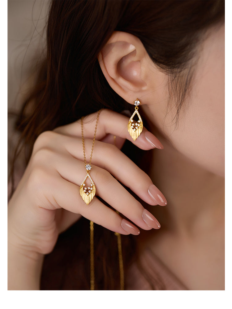 Gold earrings being worn with a hand holding one of them close to the ear.