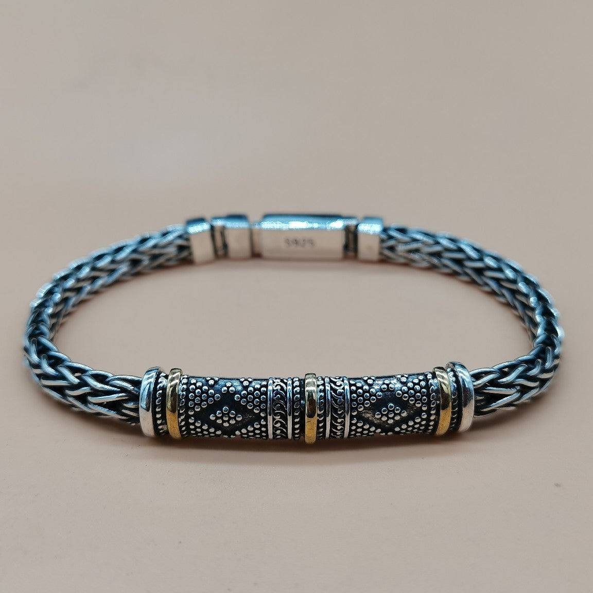 Silver braided bracelet with decorative clasp on a beige background