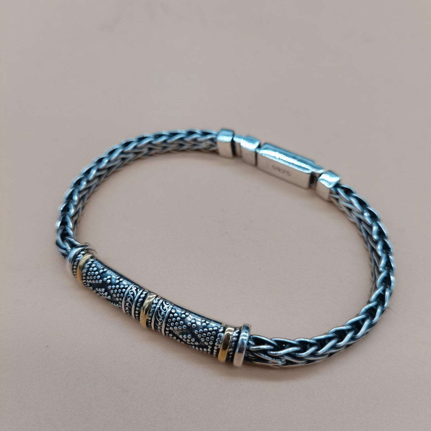 Silver braided bracelet with a decorative clasp on a beige background