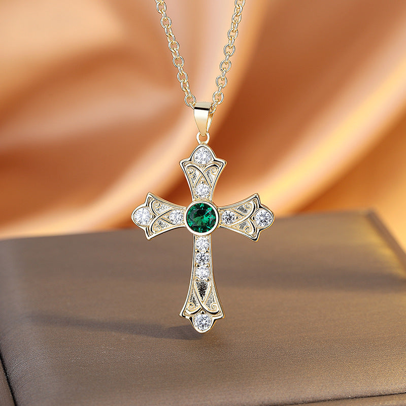 Gold cross pendant with a green gemstone on a soft fabric background