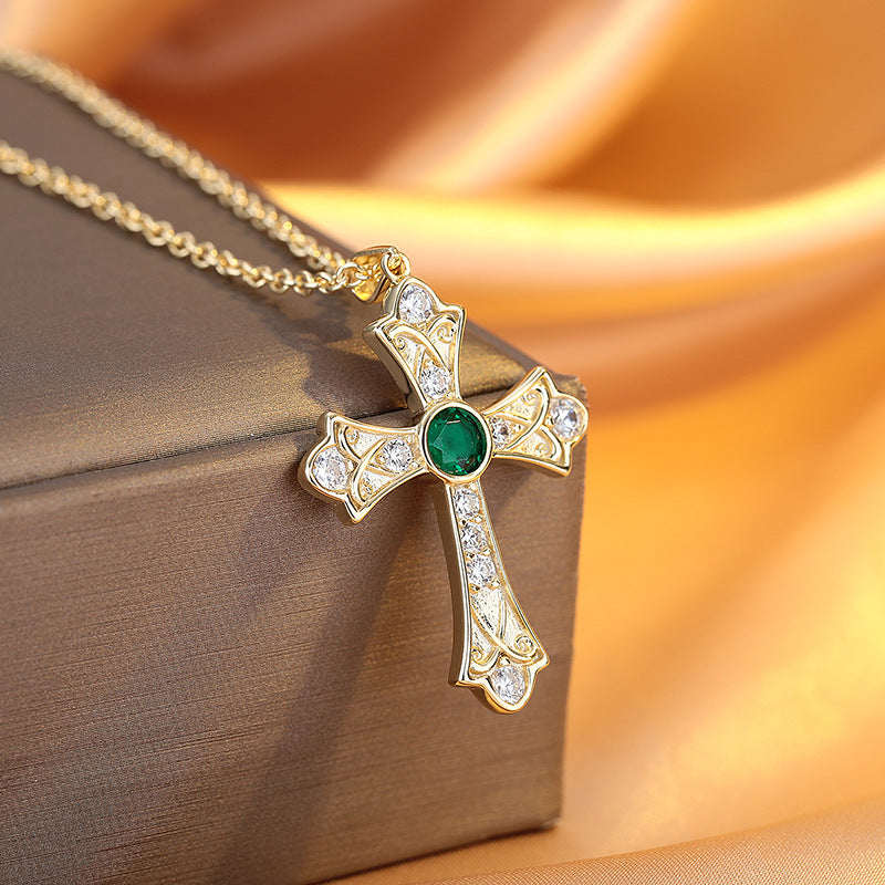 Gold cross pendant with a green gemstone on a brown fabric background