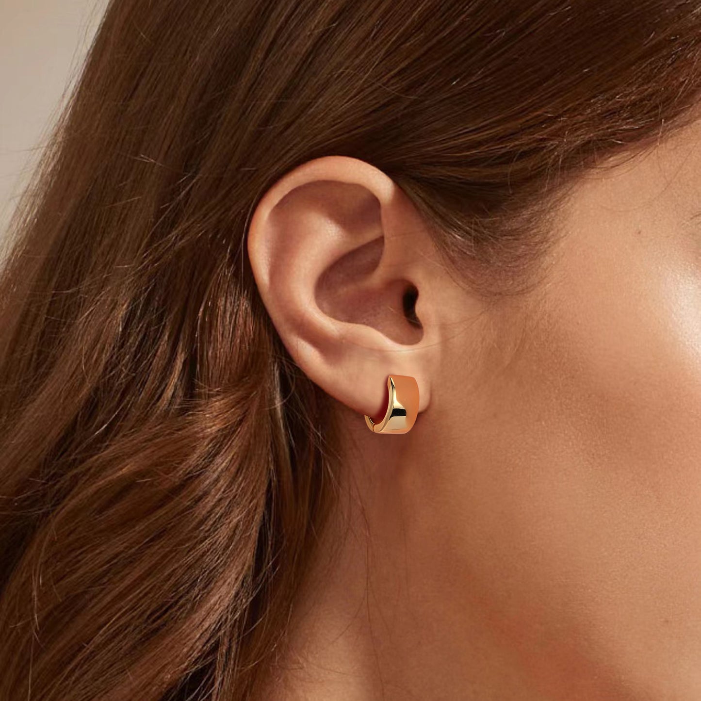 Gold hoop earring worn by a person with brown hair.
